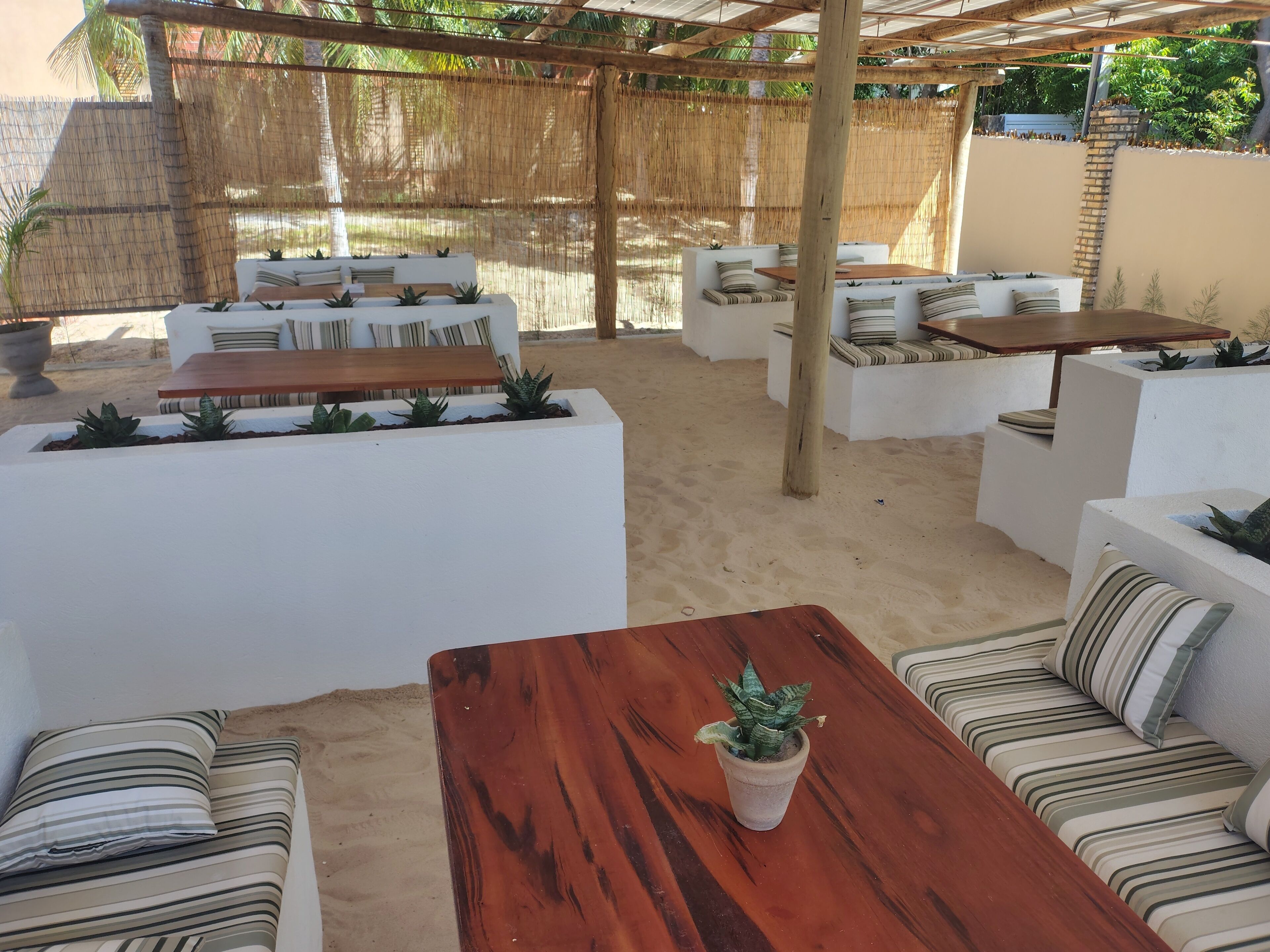 An outdoor patio with white sofas, wooden tables, and planters.
