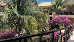 A courtyard with palm trees, bougainvillea flowers, and a tiled walkway. - Pousada Aruanã (Aracati)