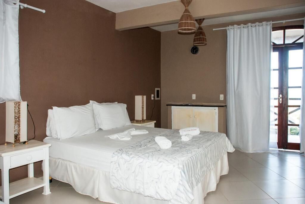 A bedroom with a bed, a nightstand, a dresser, and a window with curtains.