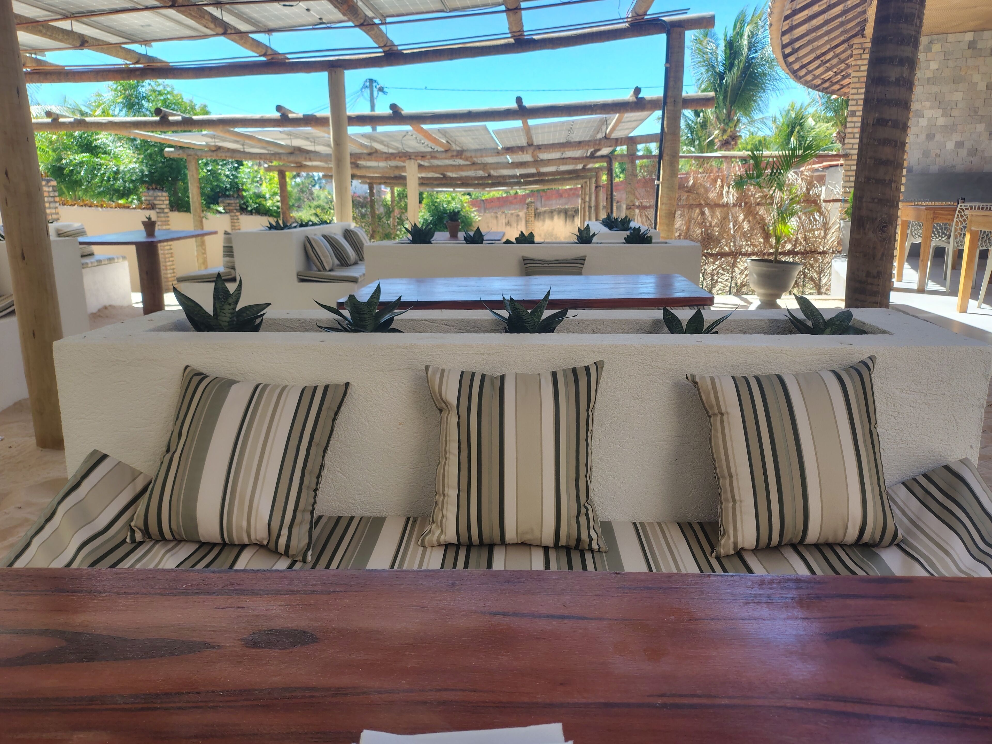 A covered outdoor seating area with a wooden table and a cushioned bench with striped pillows.