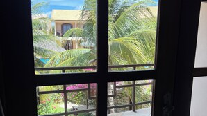 A view through a window with a view of a building, palm trees, and a tiled patio area. - Pousada Aruanã (Aracati)