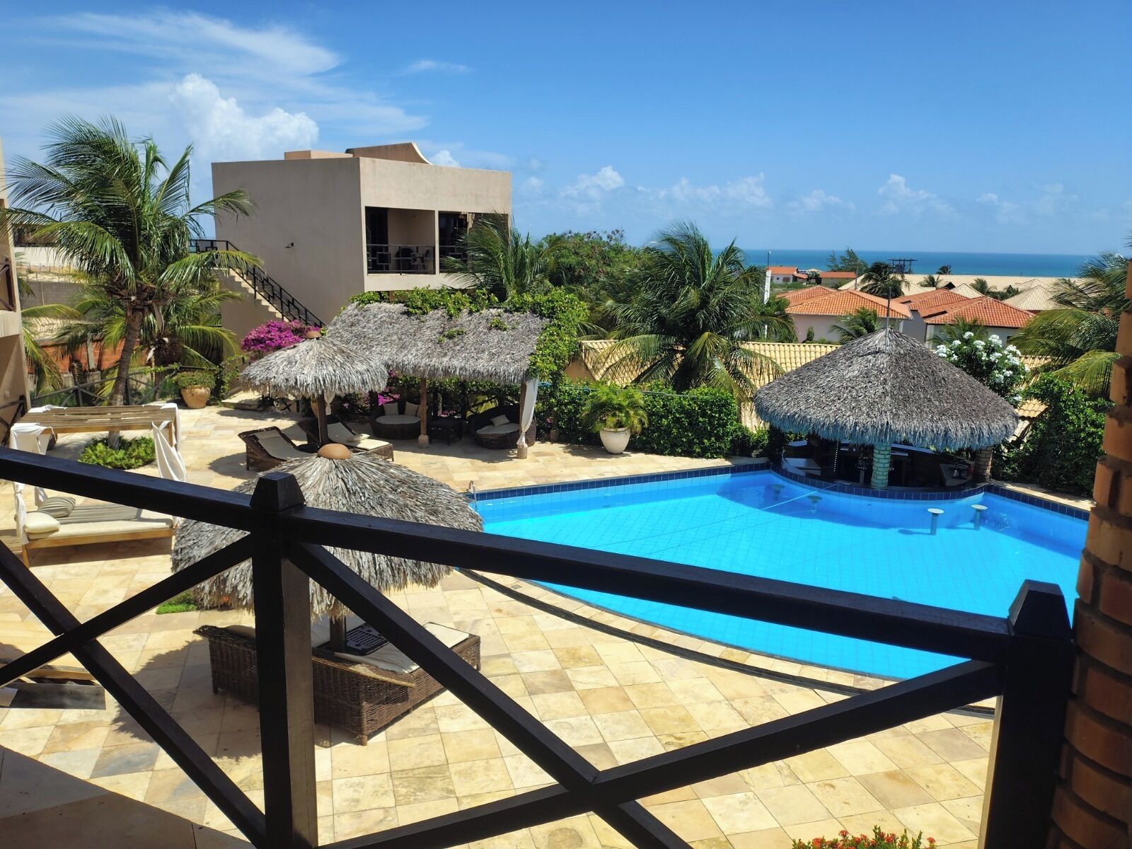 A pool area with lounge chairs and thatched umbrellas, overlooking a beach and ocean.