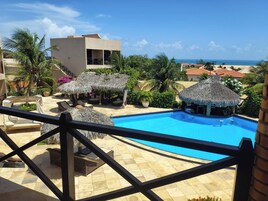 A pool area with lounge chairs and thatched umbrellas, overlooking a beach and ocean.