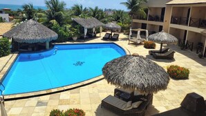 A pool area with a clear blue pool, lounge chairs, and thatched umbrellas. - Pousada Aruanã (Aracati)