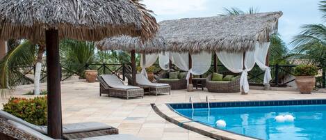 A poolside area with thatched umbrellas, wicker lounge chairs, and a swimming pool.