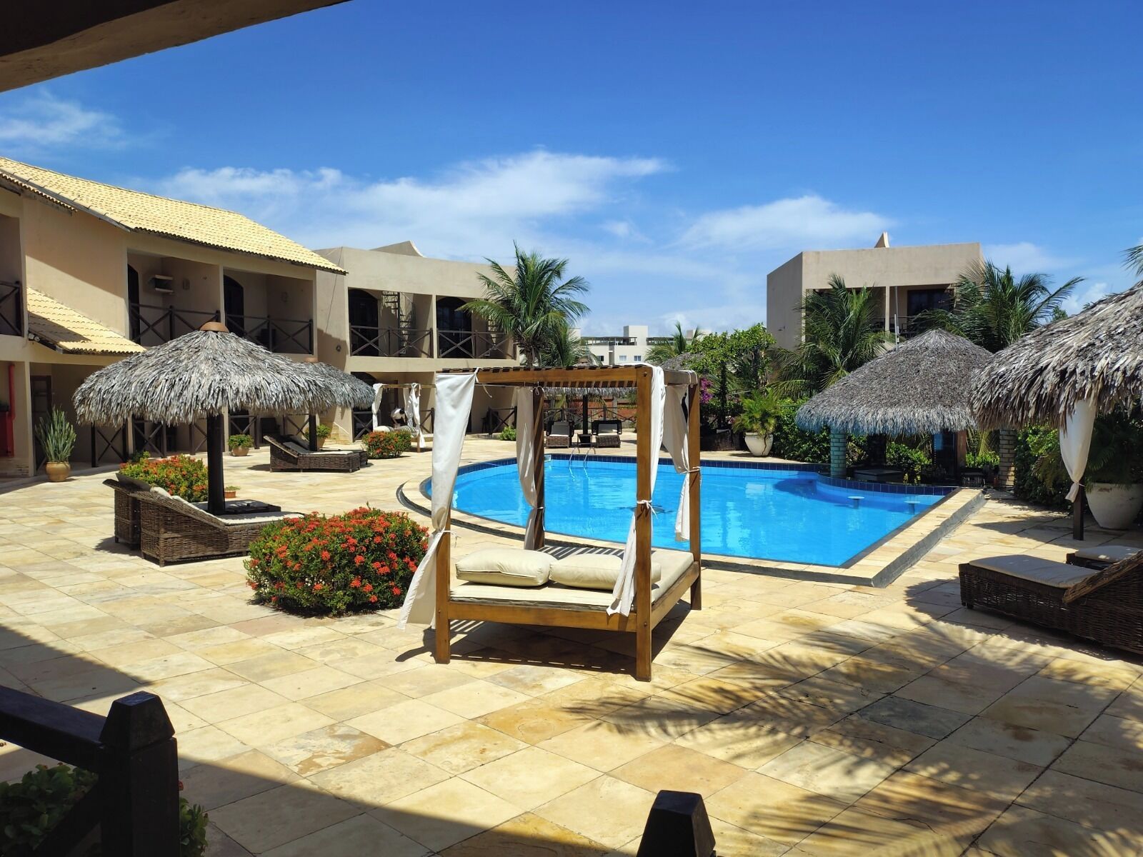 A poolside area with a clear blue pool, lounge chairs, and thatched umbrellas.