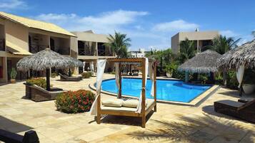 A poolside area with a clear blue pool, lounge chairs, and thatched umbrellas.