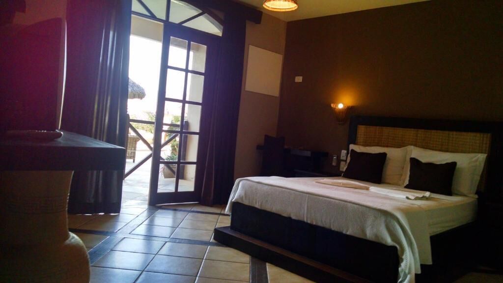 A hotel room with a bed, a chair, a table, and a view of the outdoors.