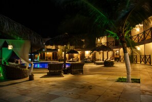 A nighttime resort with a pool, lounge chairs, and thatched umbrellas. - Pousada Aruanã (Aracati)