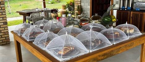 A covered outdoor dining area with a wooden table and food covers.
