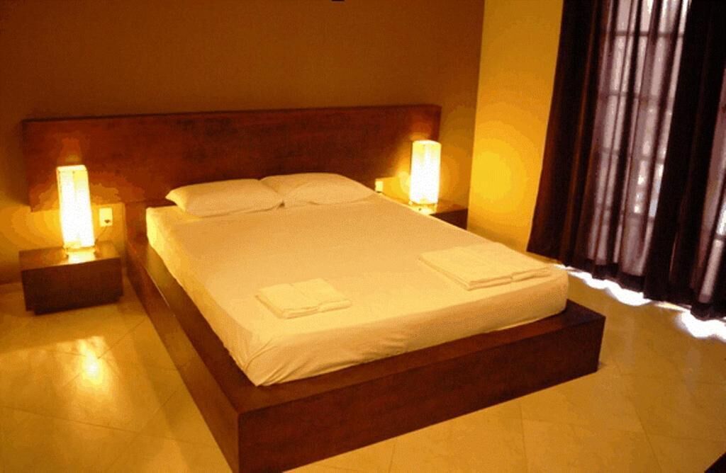 A hotel room with a large bed, two bedside lamps, a wooden headboard, and a window with curtains.