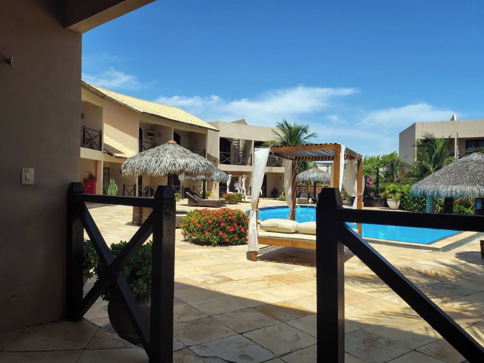 A pool area with a clear blue sky, a pool, and a covered seating area with umbrellas.