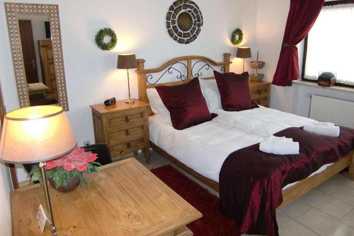 Un dormitorio ordenado con cama, mesitas de noche, lámparas y detalles decorativos en la pared.