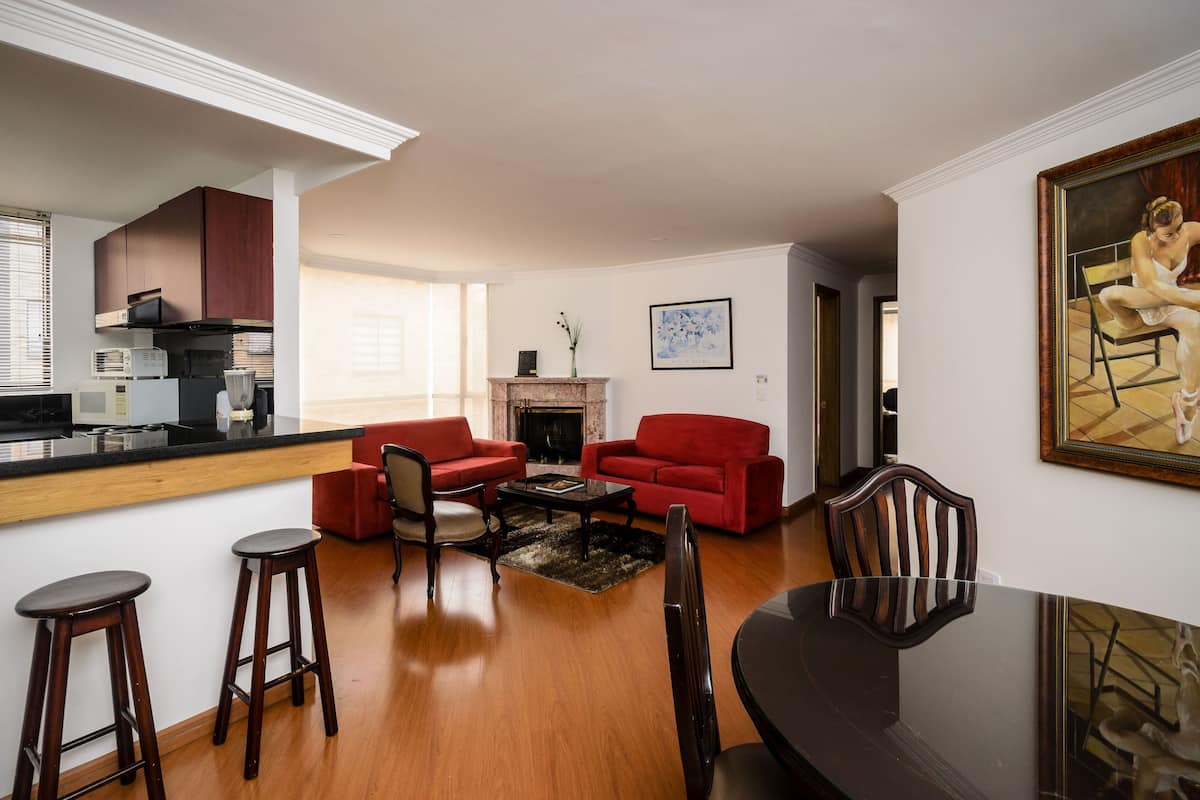 Ein modernes Wohnzimmer mit Küchenbereich, roten Sofas, einem Kamin und einem Esstisch mit Stühlen.