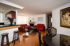 A modern living room with a kitchen area, red sofas, a fireplace, and a dining table with chairs. - Travelers Suites Edificio Fontana Plaza (Bogotá)
