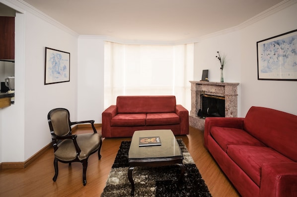 Una sala de estar con un sofá rojo, un sillón de madera y una mesa de centro de vidrio.