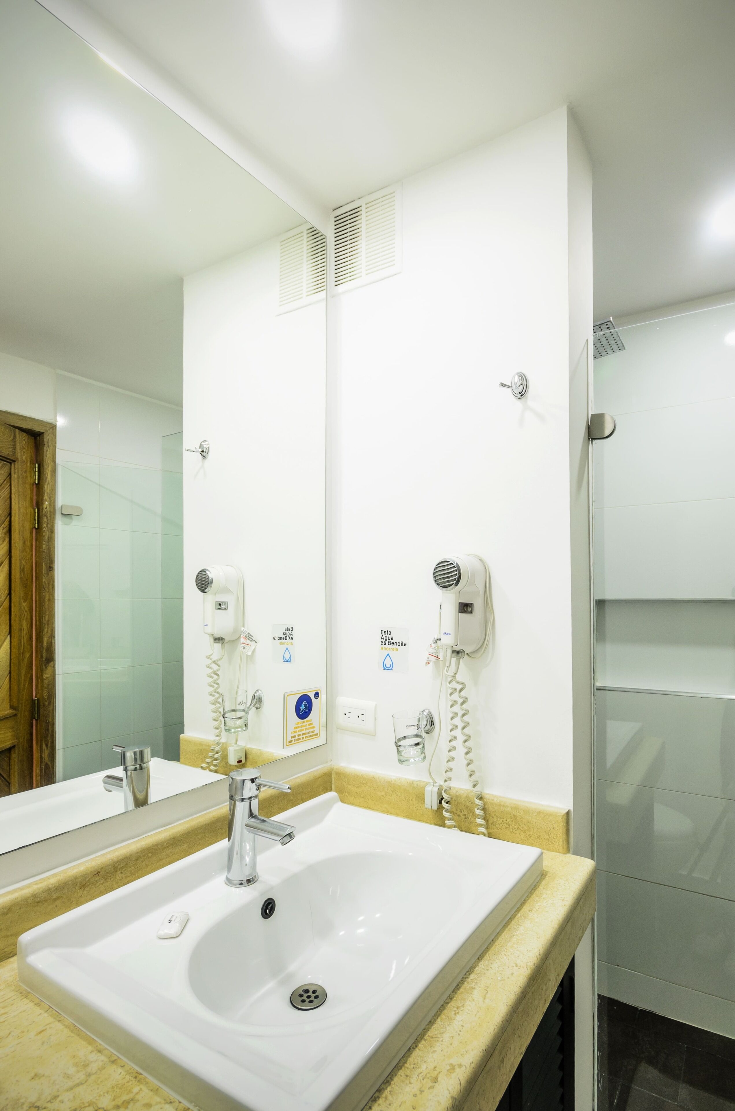 Uma casa de banho com uma pia branca, um espelho e dois secadores de cabelo fixados na parede.