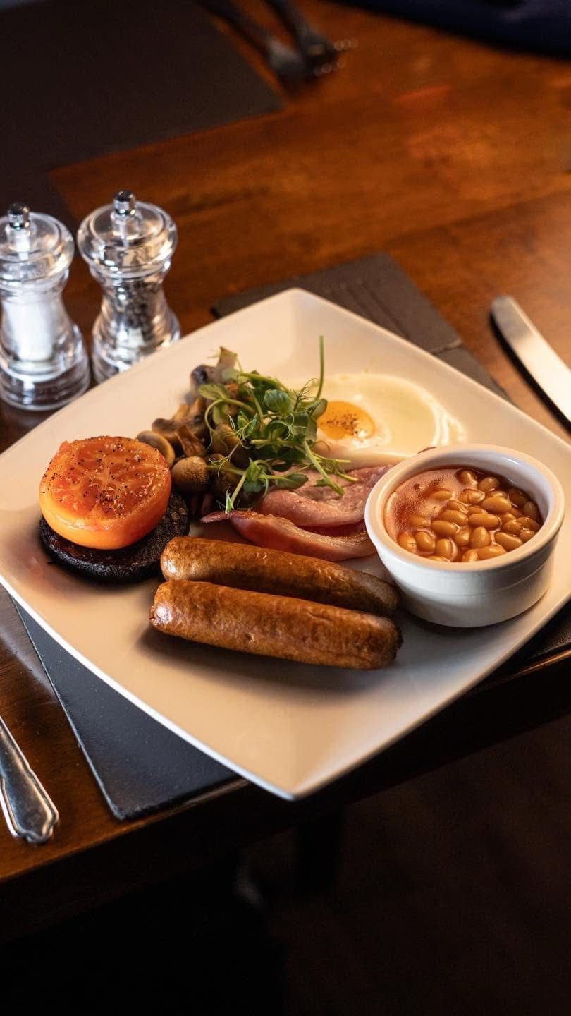 A breakfast plate with eggs, sausages, beans, a slice of tomato, and greens.