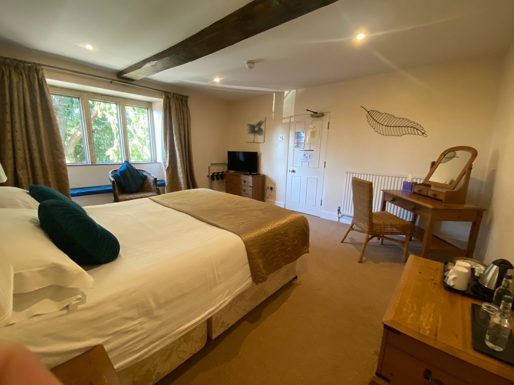 A hotel room with a large bed, a desk with a mirror, a chair, a television, and a window with curtains.