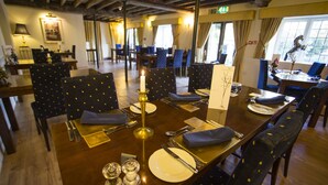 A dining area with tables set for four, featuring dark chairs with a polka dot pattern, a candle centerpiece, and a menu stand.