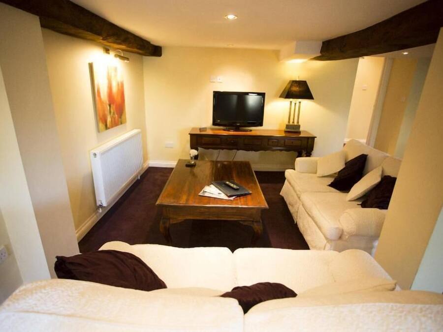 Una sala de estar con un sofá blanco, una mesa de centro de madera, un televisor y una lámpara.