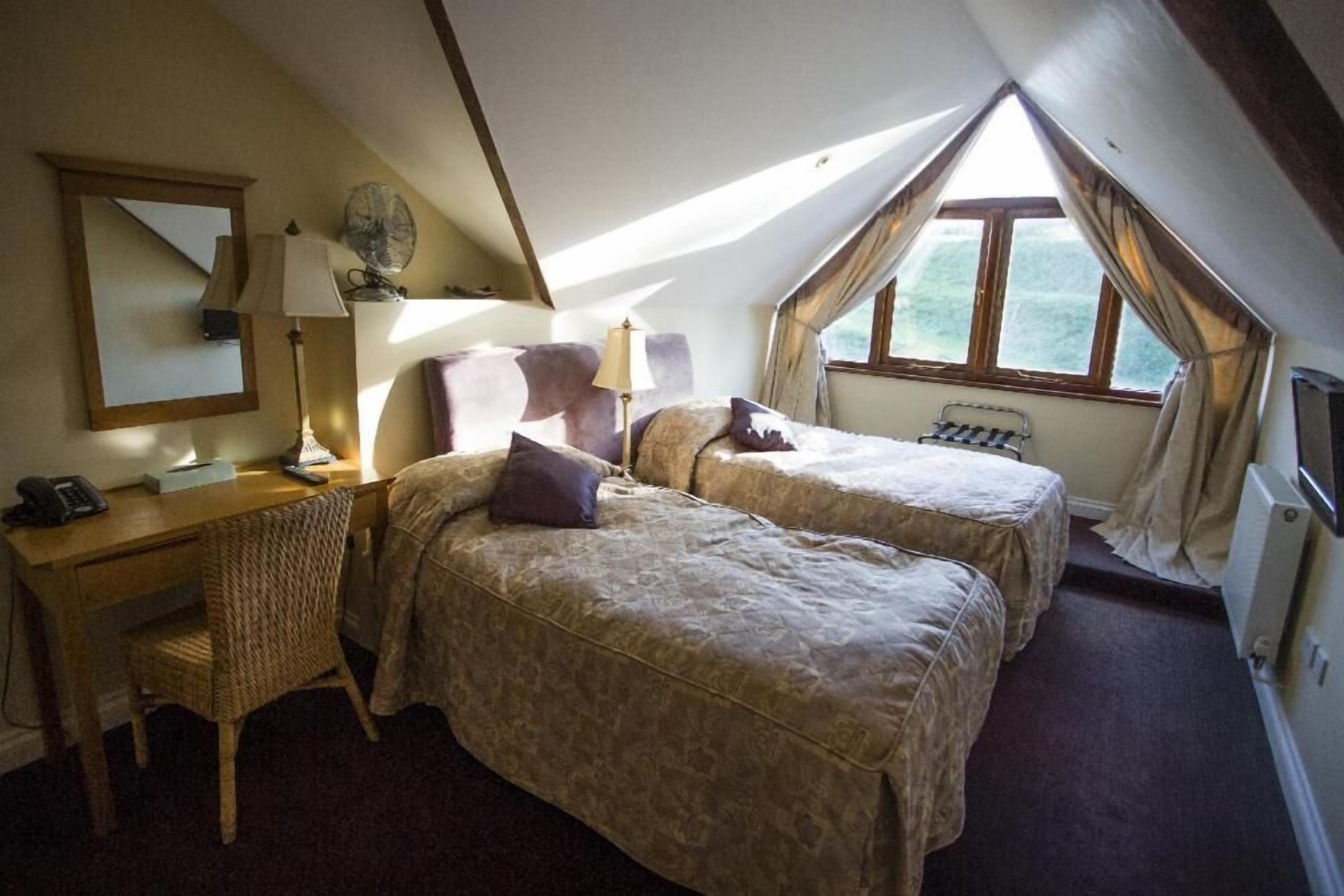 A cozy attic bedroom with two beds, a desk, and a chair.