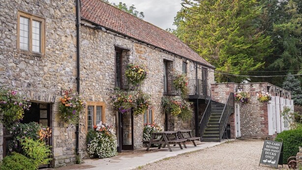 A stone building with a tiled roof, outdoor seating, and flower baskets.