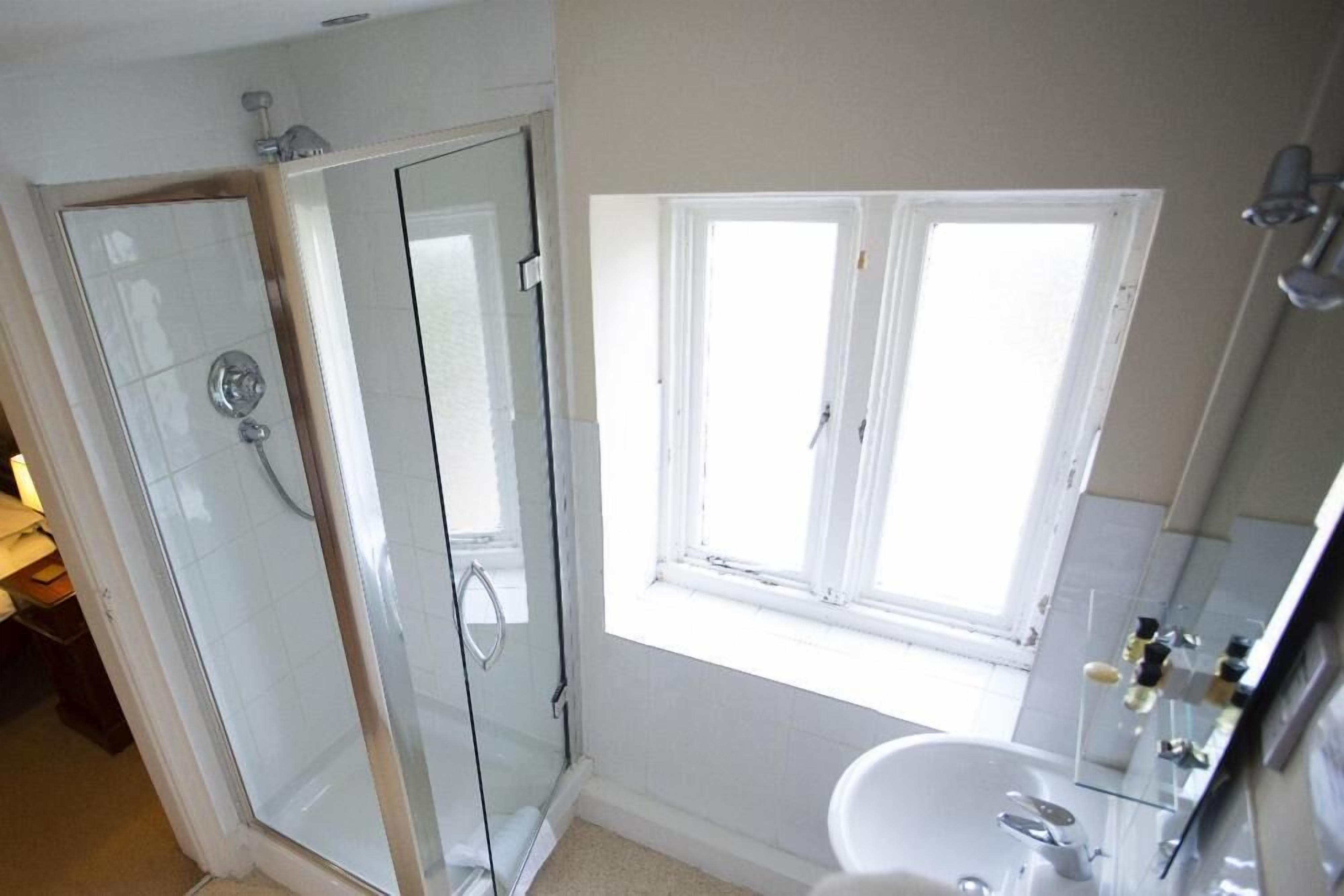 Een badkamer met een glazen douchecabine, een wastafel en een raam voor natuurlijk licht.