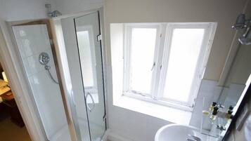 Een badkamer met een glazen douchecabine, een wastafel en een raam voor natuurlijk licht.