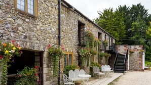 A stone building with a balcony, outdoor seating, and a staircase.