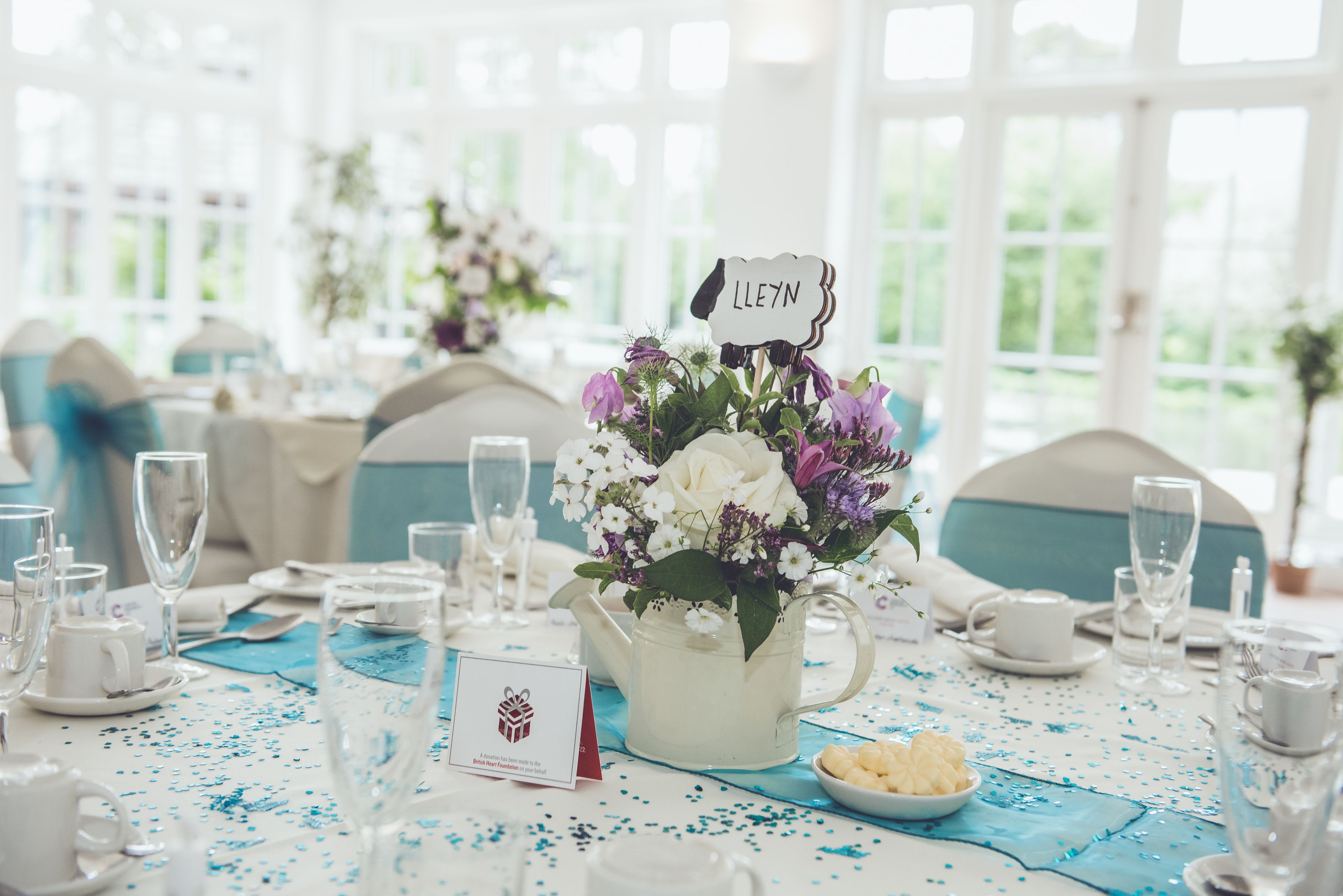 A table set for a wedding reception with a name sign, a flower arrangement, and a small bowl of snacks.