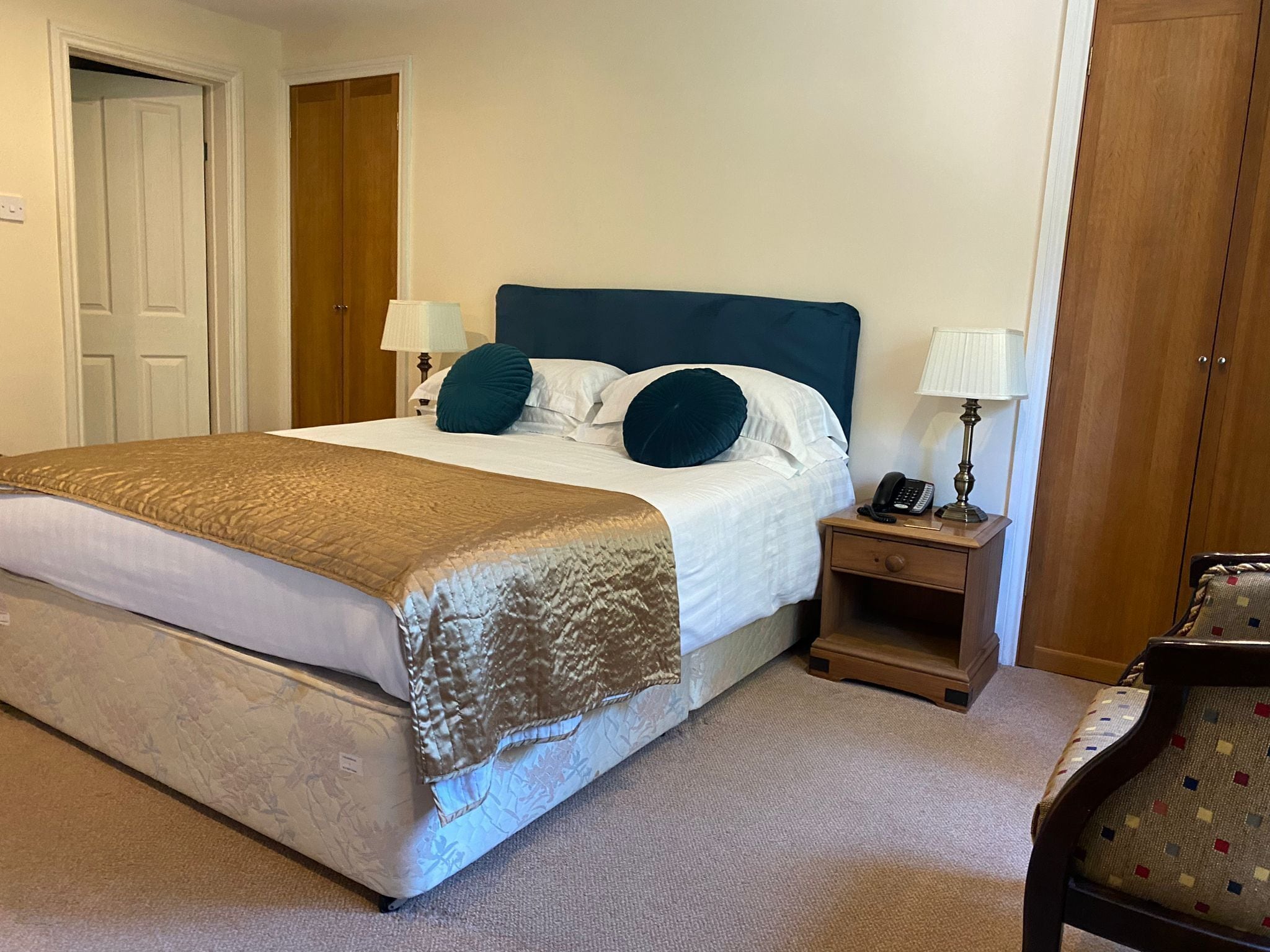 A neatly made bed with a blue headboard, two bedside lamps, and a small wooden nightstand with a phone and lamp.