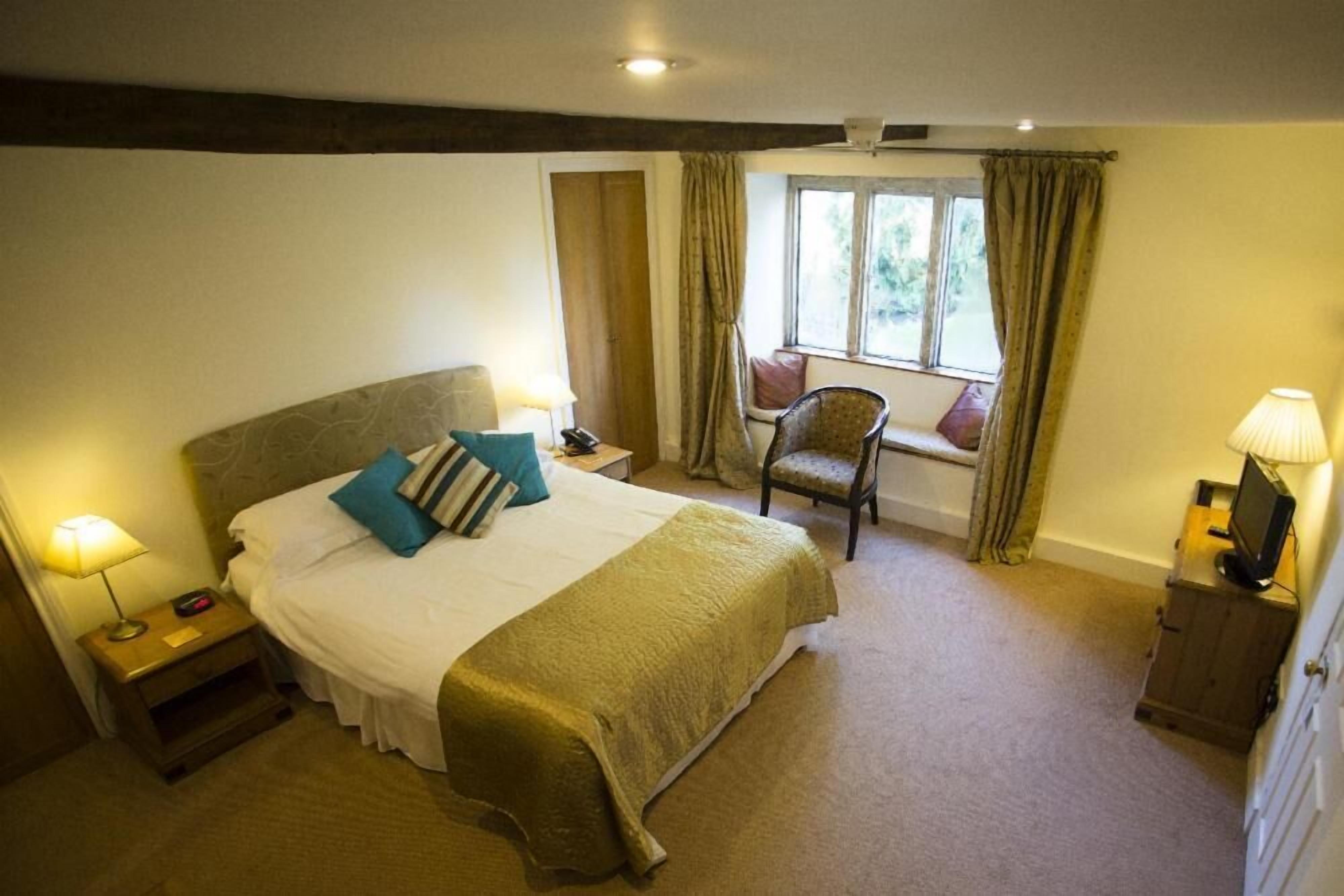 A bedroom with a large bed, a chair, a TV, and a window with curtains.