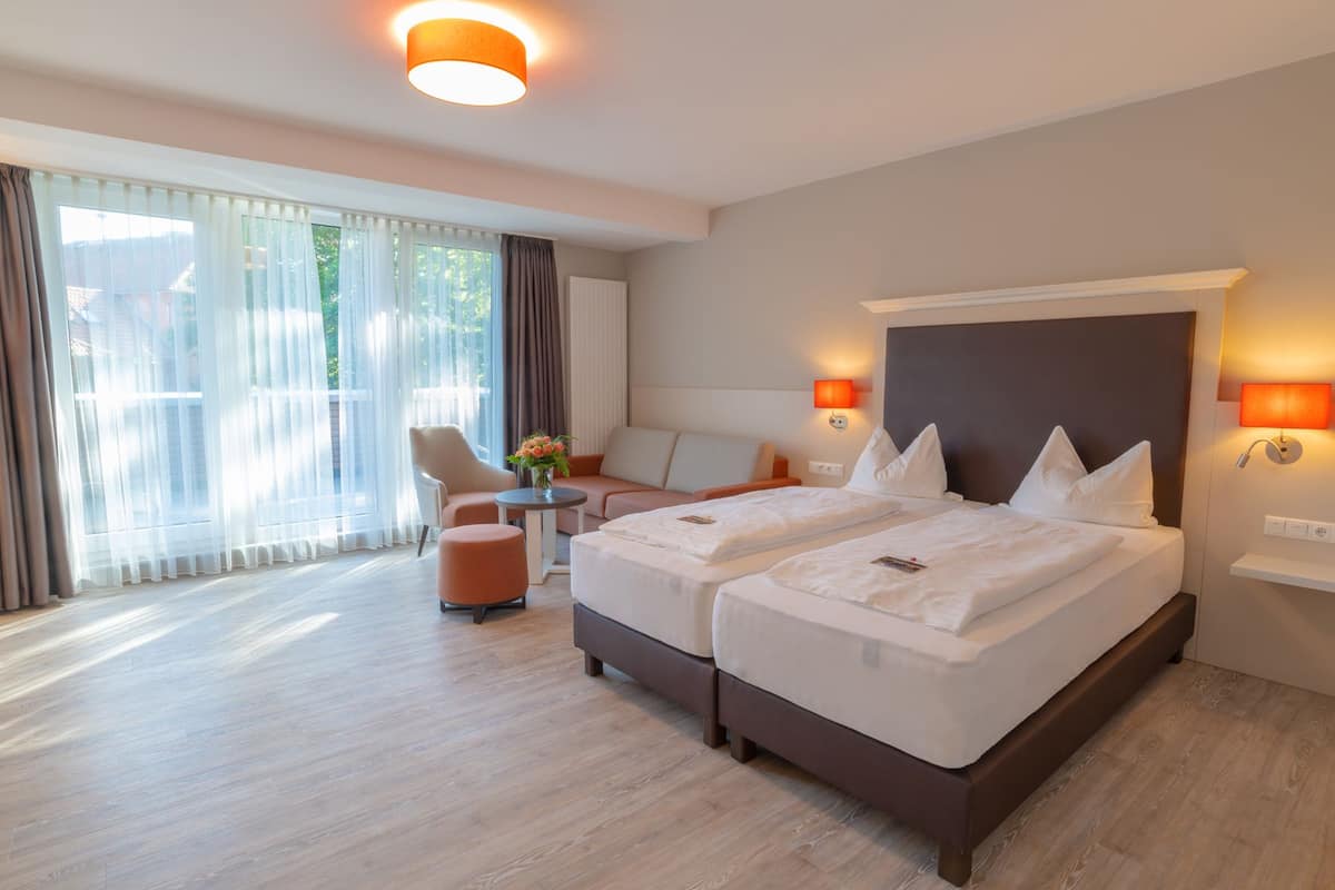 A hotel room with two beds, a sofa, a chair, a small table, and a window with curtains.