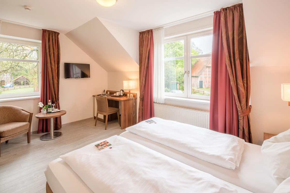 A hotel room with two beds, a desk, a chair, and a TV.