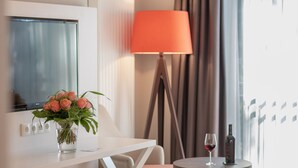 A hotel room with a bed, a bedside table with a vase of flowers, a lamp, and a small round table with a wine glass and bottle. - Flair Hotel Rieckmann (Bispingen)
