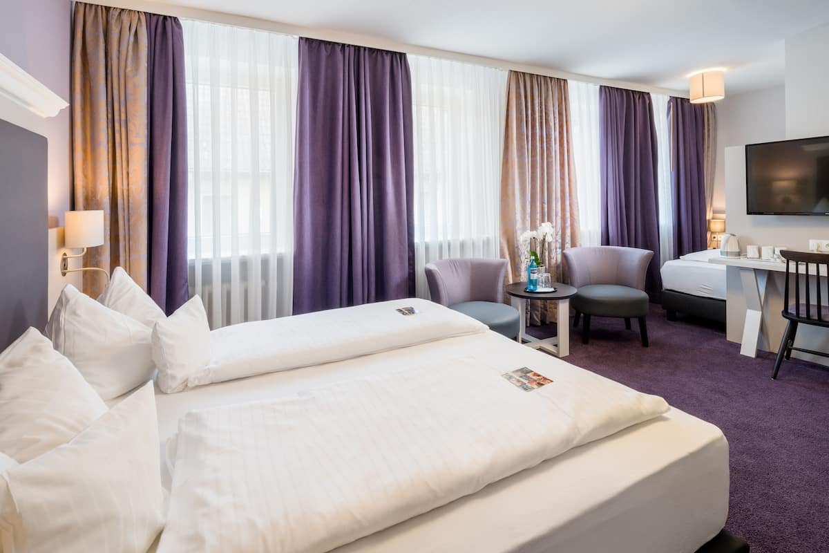 A hotel room with two beds, a desk, a chair, and a TV.
