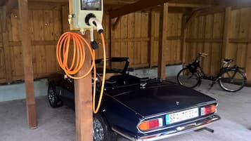 Une voiture ancienne est garée dans une grange en bois, à proximité d’une borne de recharge.