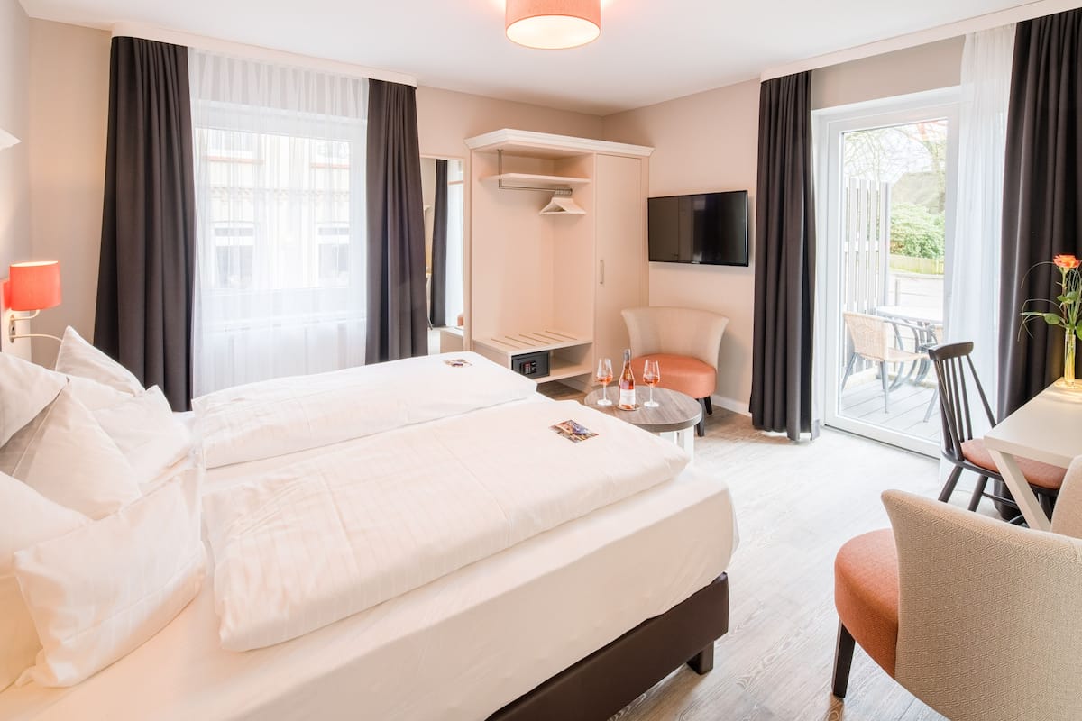 A hotel room with a large bed, a desk, a chair, a TV, and a balcony with a table and chairs.