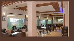 A spacious indoor area with multiple seating arrangements, including tables and chairs, and large windows providing views of the outdoors. - Hôtel El Yacouta (Tetouan)