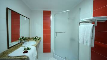 Un bagno con un piano in marmo, uno specchio grande, un lavandino bianco, un box doccia in vetro e piastrelle rosse sulle pareti.