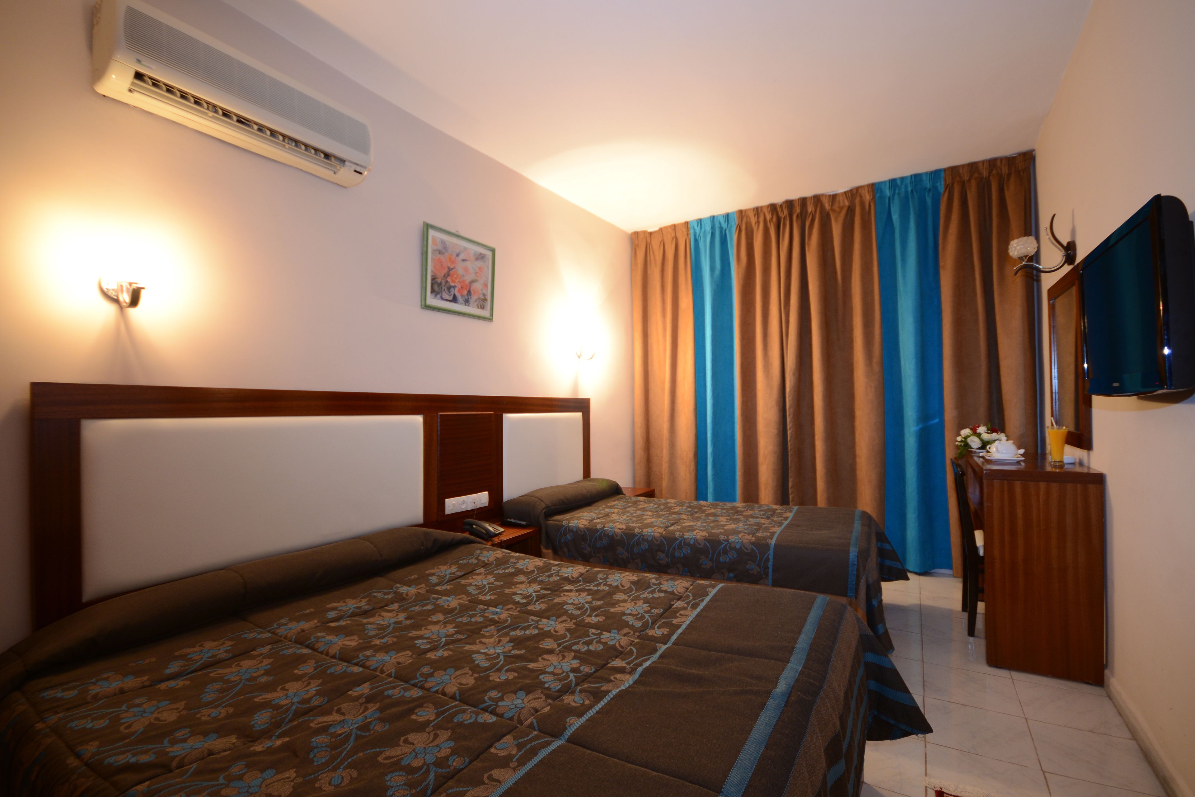 A hotel room with two beds, a desk, a TV, and an air conditioner.