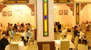 Un comedor con varias mesas y sillas, una araña y cuadros en las paredes.