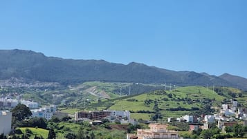 Un pueblo con edificios en una ladera, rodeado de colinas verdes y cielos despejados.