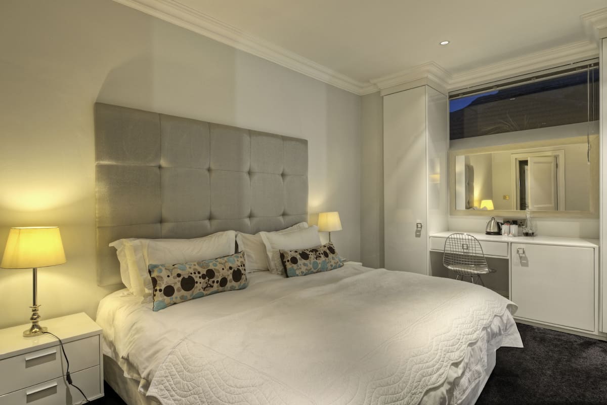A neatly arranged hotel room with a large bed, bedside lamps, a small desk, and a mirror above the desk.