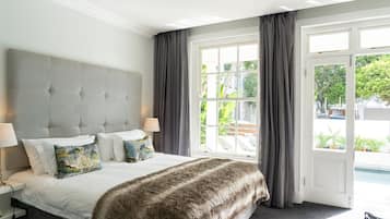 Quarto com cama grande, duas mesas de cabeceira, cabeceira estofada cinza e vista para uma piscina através de uma porta de vidro.
