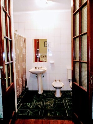 Un baño con lavamanos pedestal, inodoro pequeño y espejo.