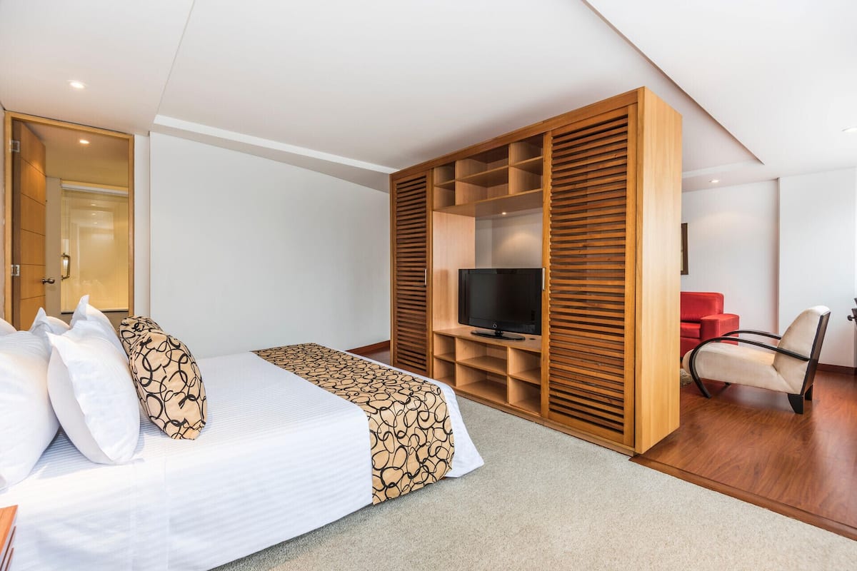Une chambre d’hôtel moderne équipée d’un lit, d’une télévision, d’un fauteuil rouge et d’une armoire en bois.