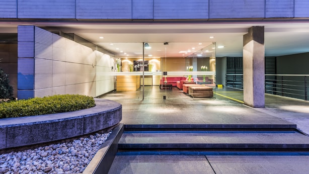 A modern building entrance with a reception area, seating, and a staircase leading to the upper floor. - Travelers Suites Obelisco Apartamentos (Bogotá)