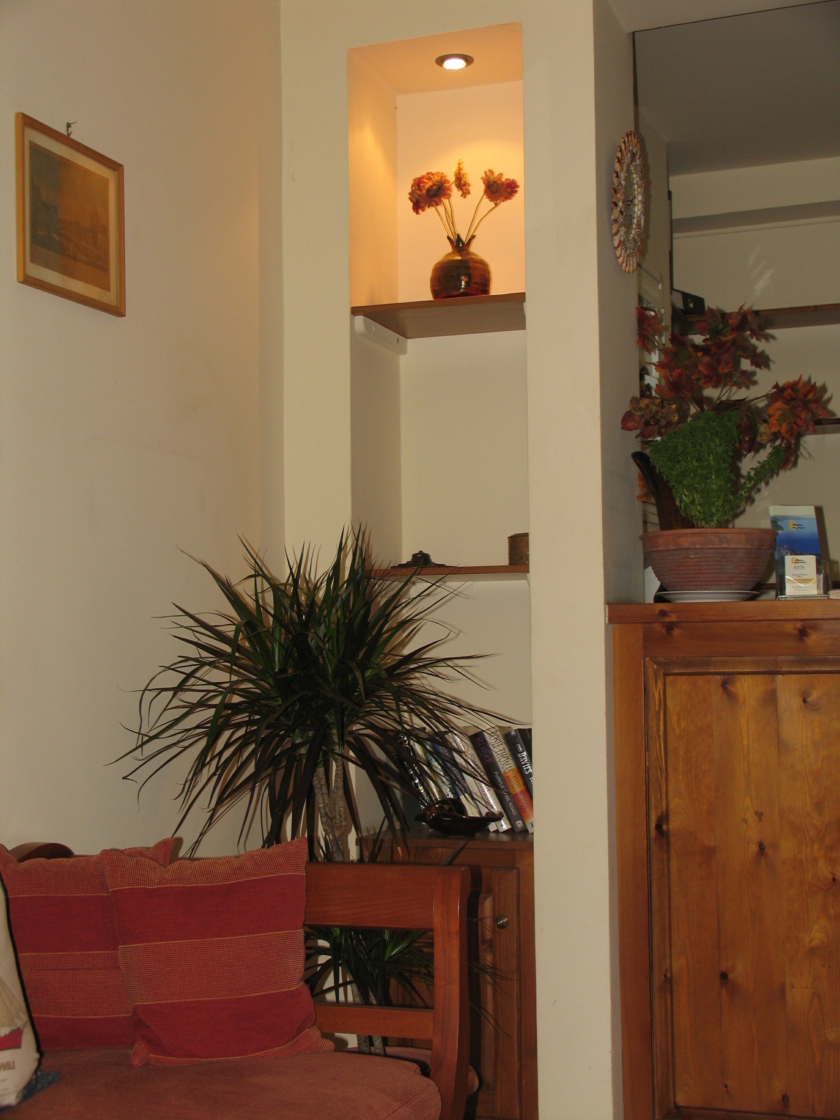 A living room with a wooden cabinet, a red sofa, a large plant, and a shelf with flowers and books.